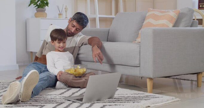 Man and his little son with laptop eating chips at home
