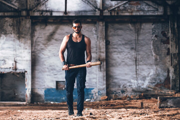 Strong Muscular Brutal Man in Black Tank Top with Baseball Bat Walks in Empty Grunge Hall