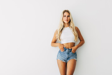 Smiling young blond hair woman holding hands on hips and looking at camera while standing against grey background - obrazy, fototapety, plakaty