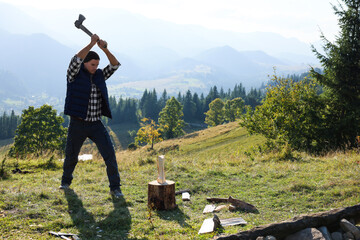 Handsome man with axe cutting firewood on hill
