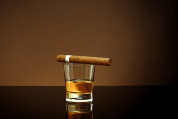 Closed up view of glass of whiskey with cigar on brown back