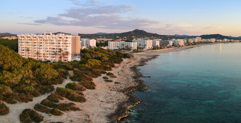 The coast of the town of Cala Millor on the east coast of the Spanish Mediterranean island of Mallorca. It's after sunrise. In the foreground are bushes and in the background the mountains.