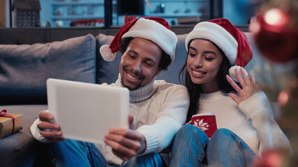 happy african american man near woman waving hand and looking at digital tablet during video call