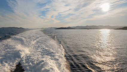 View of the sunset from the stern of the high-speed ferry. The mountains of the Mediterranean island of Ibiza can be seen on the right. The catamaran creates a long stern wave.