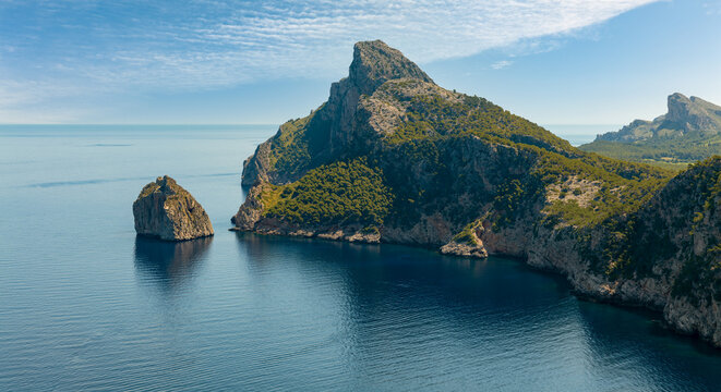 The mighty cliffs of the Formentor peninsula in the east of the Mediterranean island of Mallorca. It's a sunny day with beautiful clouds in the sky and some haze in the air.