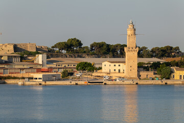 Obraz premium In the morning after sunrise in the port of Palma on the Mediterranean island of Mallorca. A lighthouse made of stones stands behind the quay wall. Sailboats are on land.