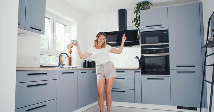 Young woman listening to music with headphones wearing pyjamas drink coffe and dance happy in the kitchen