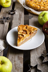 A piece of apple pie on a white plate on a wooden background. Selective focus front view.