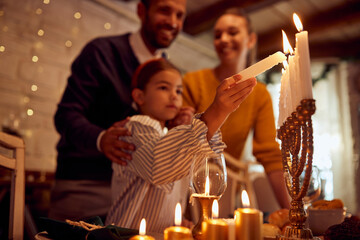Close-up of Jewish girl lights candles in menorah during family meal on Hanukkah.