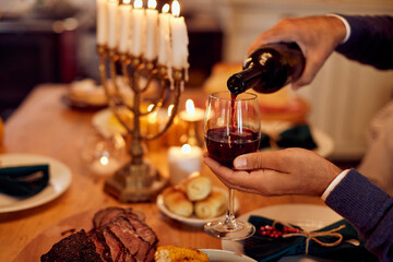 Close-up of Jewish man pours wine while having meal at dining table on Hanukkah.