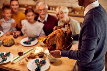 Fototapeta na wymiar Close-up of man serves Thanksgiving turkey while having meal with his family at home.