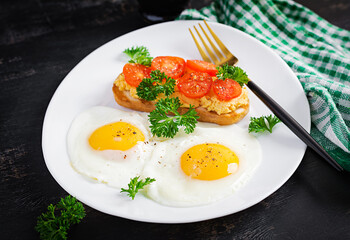 Fried eggs and a grilled chicken pate  sandwich on a dark background.