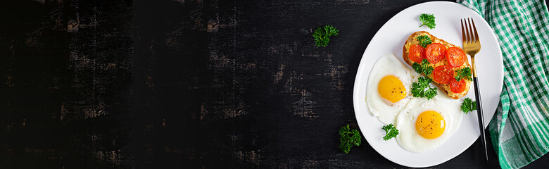 Fried eggs and a grilled chicken pate  sandwich on a dark background. Top view, banner, overhead