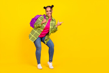Full length photo of joyful positive afro american woman wear bag point finger empty space isolated on yellow color background