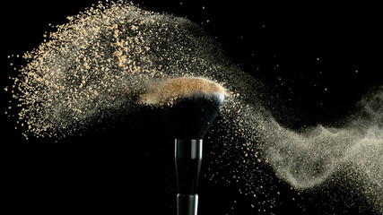 Soft cosmetics brush releasing a cloud of beige face powder.