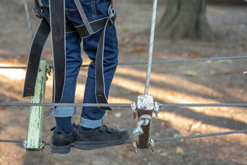 Close up of child's legs climbing on high rope park. Adventure climbing high wire park. Hobby, active lifestyle concept.