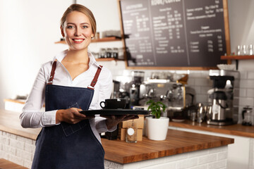 The girl waitress carries a cup on a tray.