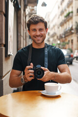 Smiling guy taking pictures on photo camera in street cafe