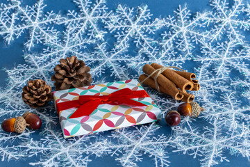 Gift box with red bow, pine cone, cinnamon branch, on snowy background.