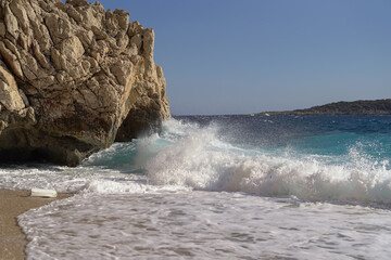 Beach in Turkey with fine yellow sand and azure water, waves crashing against the rock