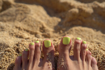 Bright light green summer pedicure on the toes of a girl on the beach against a background of sand