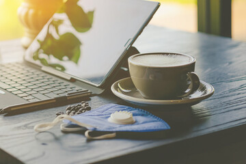 Hot Cappuccino coffee with protective face mask for people work from home by using laptop and stress relief with hot coffee on a table. Concepts of Covid-19 (Coronavirus). Selective focus on coffee.