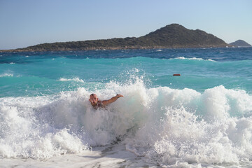 Young tattooed sporty man on the beach on a hot summer sunny day, playing with waves, jumping, having fun