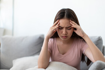 Asian young woman holding her hands on the forehead and have a headache on the sofa.