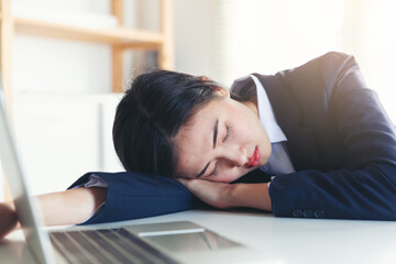 Tired business woman sleeping near laptop while working at office desk in her office, hard work and overworked