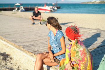 Two young women sitting on the beach with a summer windy day and cute chatting talking