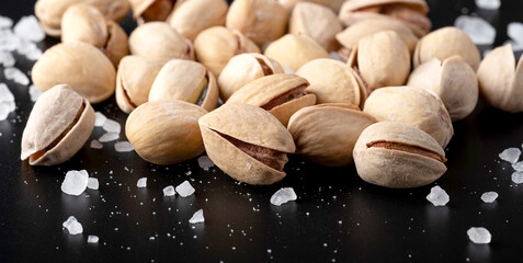 Beautiful salted pistachios with large grains of salt on a black mirror background with reflection. Close-up. Front view