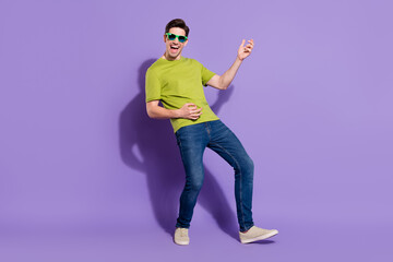 Fototapeta na wymiar Full size photo of cool young brunet guy play guitar wear t-shirt jeans shoes eyewear isolated on violet background