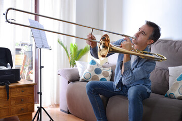 Novice man playing trombone at home with enthusiasm