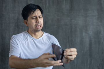 Asian man wearing a white t-shirt Looking empty wallet no money with shock