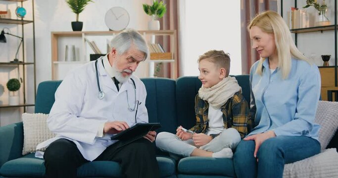 Child healthcare concept where handsome friendly skilled respected bearded doctor talking with his positive boy patient with sore throat and giving him high five during home visit