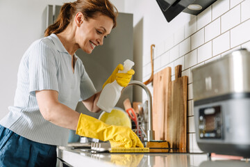 Ginger mature woman smiling while cleaning sink in kitchen