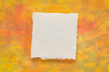 small sheet of blank white Khadi rag paper from South India against orange and yellow marbled paper