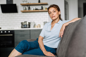 Ginger mature woman looking ahead while sitting on couch