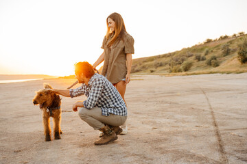 White young couple smiling and stroking their dog while walking together