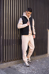 Fashionable man in beige costume and vest posing near wall