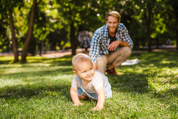 Naklejka na ściany i meble White father playing with his son while resting on grass