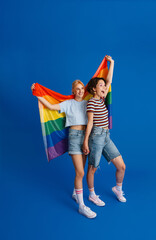 Excited lesbian couple holding hands while posing with rainbow flag