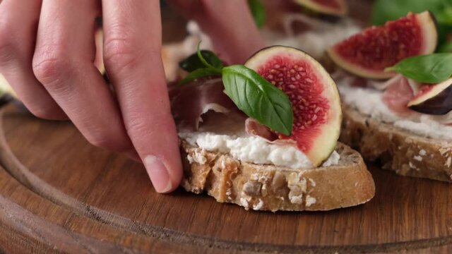 Fig prosciutto bruschetta decorated with basil and honey on wooden serving board, closeup view
