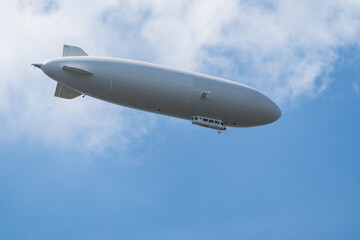 Naklejka na ściany i meble Gray cigar-shaped airship flying in blue sky under clouds