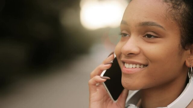 Portrait of attractive Afro American girl having phone talk. Young beautiful girl at the street. Happy smiling girl walking forward. High quality 4k footage