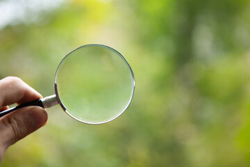 hand holding a magnifying glass on the background of nature