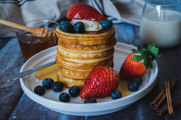 Closeup view of Stack of pancakes with honey, strawberry, blue berry and whip cream on top in plate, delicious dessert with milk