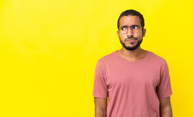 Obraz premium Young latin man isolated on yellow background having doubts while looking side