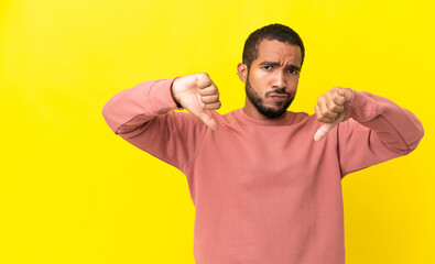Young latin man isolated on yellow background showing thumb down with two hands