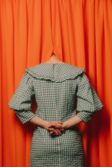 girl in a green dress hides her head in orange curtains